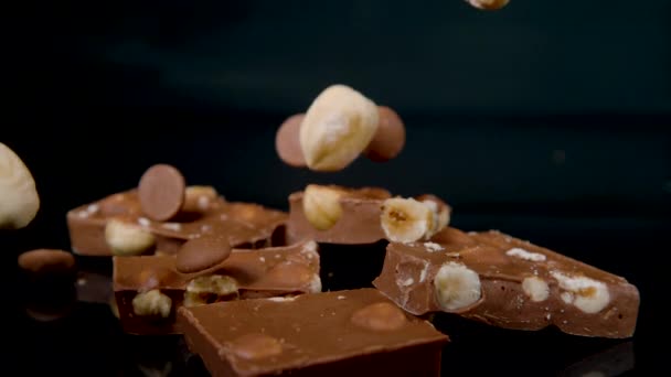 MACRO: Hazelnuts and cocoa drops fall over a pile of chocolate with hazelnuts — Vídeo de Stock