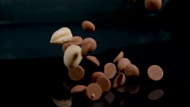 MACRO: Ένα μείγμα από ασπρισμένα φουντούκια και σταγόνες σοκολάτας γάλακτος σκορπίζεται. — Αρχείο Βίντεο