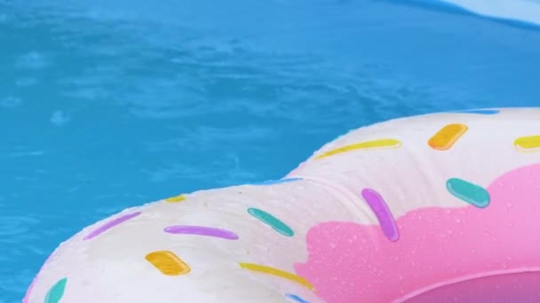 CLOSE UP: Regen ergießt sich auf einen aufblasbaren Donut, der im Pool schwimmt. — Stockvideo