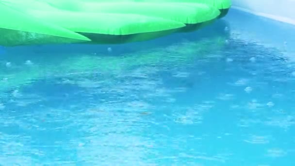 CLOSE UP: Дощ починає падати на надувний лист, що плаває навколо басейну . — стокове відео