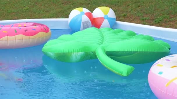 CERRAR: Hoja inflable, donas y bolas flotan alrededor de una piscina durante la tormenta de lluvia — Vídeos de Stock