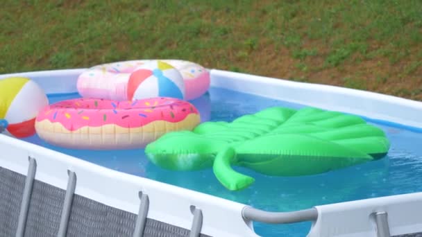 Pequeña piscina patio trasero se deja lleno de coloridos flotadores durante una tormenta de verano. — Vídeos de Stock