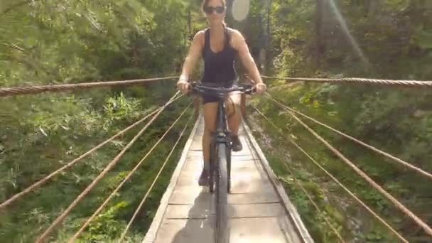 FECHAR UP Jovem mulher monta uma bicicleta elétrica através de uma ponte de suspensão simples — Vídeo de Stock