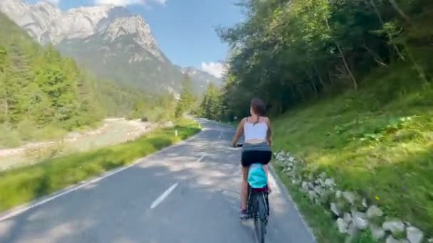 山の中で休暇中の女性はアスファルトの道路を電動自転車に乗る. — ストック動画