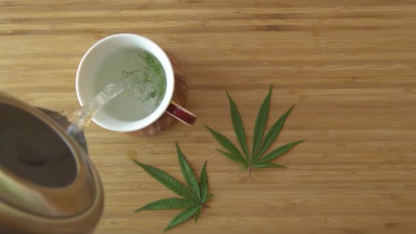Kokande vatten hälls över ett marijuanablad inuti en vit tekopp.. — Stockvideo