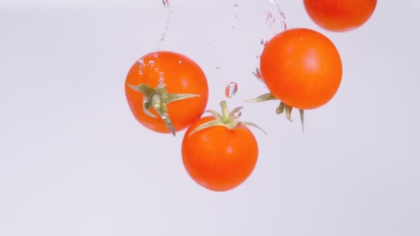 CLOSE UP: Lebendige rote Kirschtomaten fallen ins glasklare Süßwasser. — Stockvideo