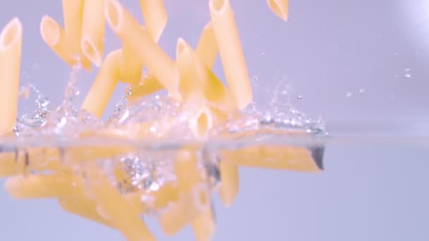 HALF ONDERWATER: droge penne pasta valt in een pot vol kristalhelder water. — Stockvideo