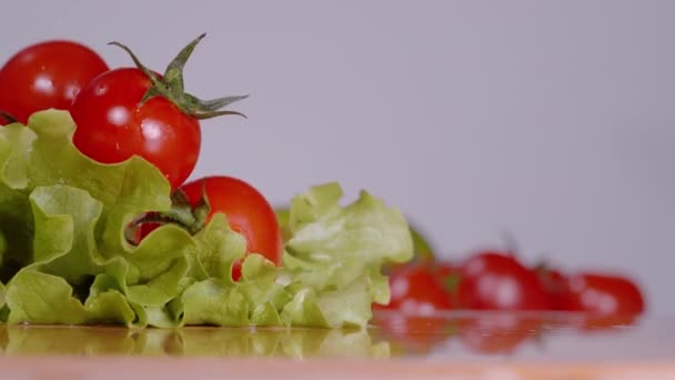 MACRO: Tomates cereja cair sobre folhas de alface romaine molhadas em tábua de cortar. — Vídeo de Stock