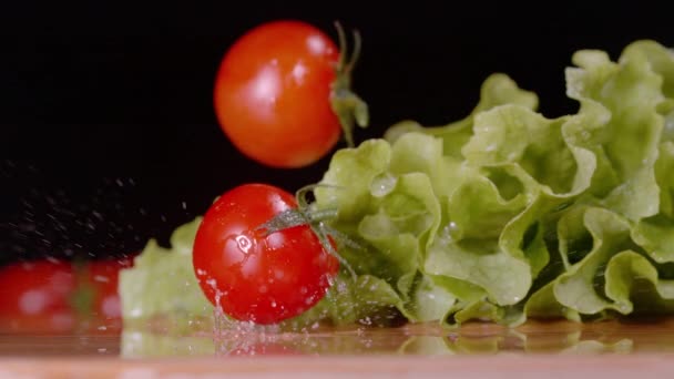 MACRO: Los tomates rojos brillantes caen y aterrizan sobre las hojas húmedas de lechuga romana. — Vídeo de stock