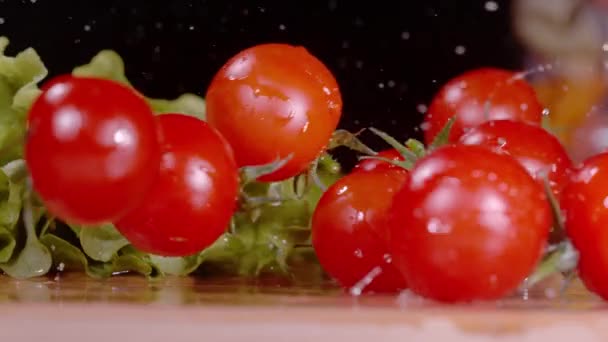 MACRO: Вода брызгает, как промытые помидоры черри катятся по разделочной доске. — стоковое видео