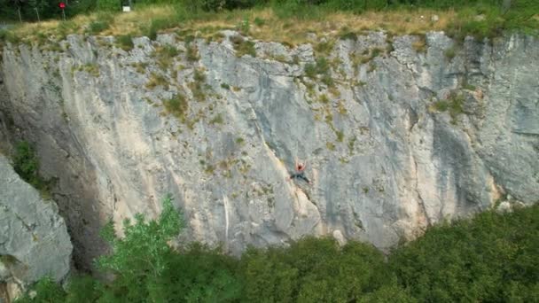 AERIAL: Lecąc nad skałą kobiety wspina się po skalistym klifie w wiejskiej Słowenii. — Wideo stockowe