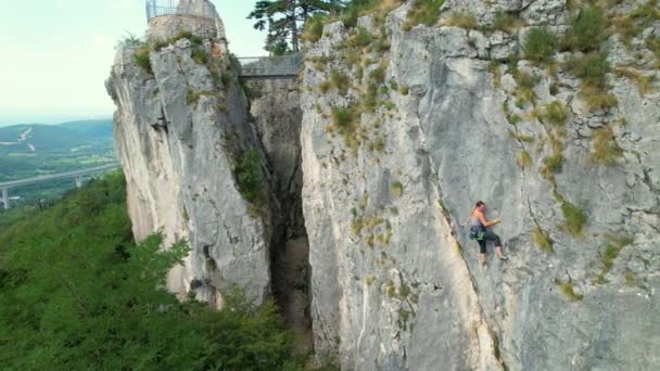 AERIAL: Drohnenblick einer Bergsteigerin beim Aufstieg auf eine herausfordernde Klippe. — Stockvideo