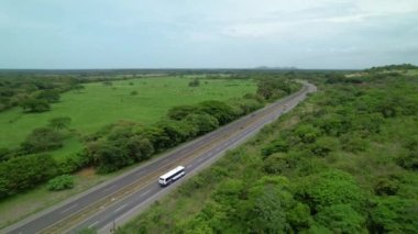Beyaz otobüs, bulutlu bir öğleden sonra Panama 'nın canlı ormanlarından geçen manzaralı bir otobanda ilerliyor. İnsansız hava aracı, dünyaca ünlü Pan-Amerikan Otoyolu boyunca hafif trafik akışına bakıyor..