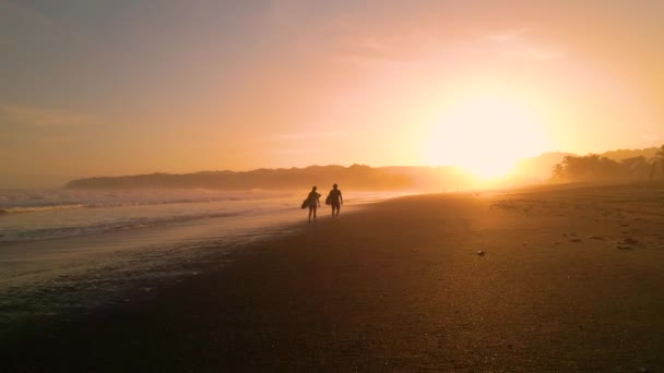 Silhouette Aerial Seguindo Dois Surfistas Andando Pela Praia Carregando Pranchas — Vídeo de Stock