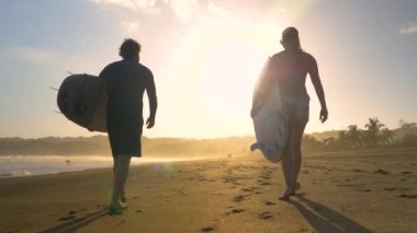 SLOW MOTION, LOW ANGLE VIEW: Following surfers walking on a sandy beach with surfboards. Two friends going surfing at sunset on Playa Venao surf spot. Beach lifestyle shot in beautiful golden light.