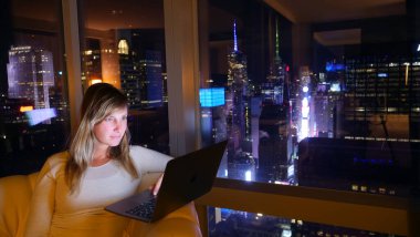 Times Meydanı 'nın yukarısındaki otel odasından laptopuyla çalışan bir kadın. New York şehir merkezinin çarpıcı manzarası ile ofisinde fazla mesai yapan beyaz bir iş kadını..
