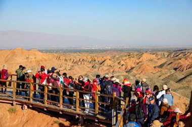 RAINBOW MOUNTAINS, ÇİN; ECTOBER 2018: Meşhur Gökkuşağı Dağları 'nın çarpıcı manzarası ile ahşap yürüyüş yolu boyunca hareket eden turistler. Bir sürü gezgin Zhangye 'deki bir jeolojik parkı dolduruyor..