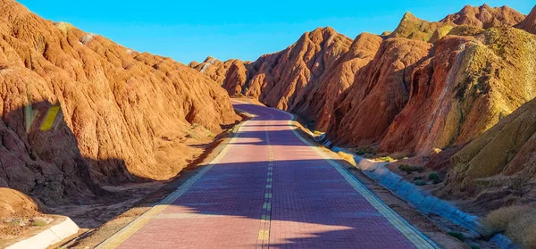 Red cobbled road runs through the beautiful Zhangye Danxia Landform in China. Scenic road offers a scenic view of the Rainbow Mountains. Path leading across the stunning Danxia sandstone landform.