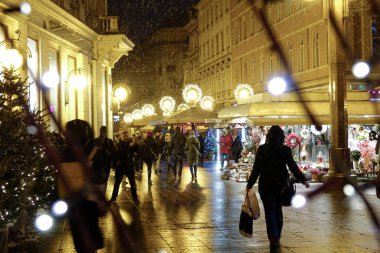 Yaklaşan DOF: Turistler soğuk bir kış akşamında Zagreb şehir merkezinde cennet gibi pazarların önünden geçtiler. Noel ışıklarının ve turistlerin resimli yeni yıl pazarını keşfettikleri bir resim.