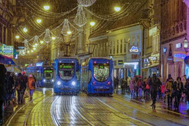 ZAGREB, CROATIA, Aralık 2018: Turistler ve yerliler kışın Avrupa 'nın pitoresk şehrini keşfetmenin tadını çıkarıyorlar. Zagreb sokaklarından geçen tramvaylar, sakin bir kış akşamında.