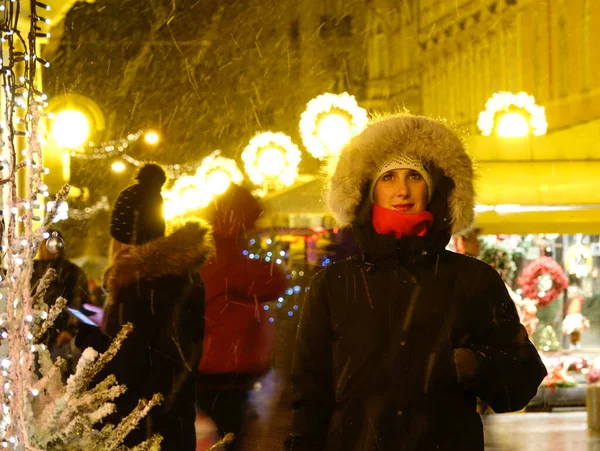 閉じる Dof 12月の雪の夜に風光明媚な出現市場の周りに楽しい女性観光客が見えます かなり白人女性はクリスマスマーケットのお祝いのライトや市場の屋台に魅了されています — ストック写真