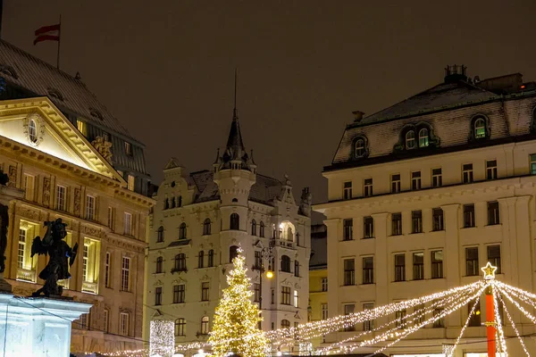 閉じる クリスマスライトや装飾品は ウィーンの歴史的な建物を照らします 冬の休暇中に古いヨーロッパの建築物の絵のような景色 牧歌的な新興市場の上の建物 — ストック写真