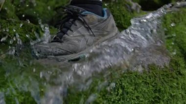 KAMNISKA BISTRICA RIVER, SLOVENIA, EYLÜL 2020: Yavaş hareket, Yaklaş, Reebok ayakkabıları giyen tanınmayan yürüyüşçü, kristal berrak orman deresine adım atıyor. Nehre adım atan kişi