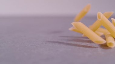 Süper Yavaş Hareketler, Yaklaş, Sonda lensleri: Gri arka planda yayılmış makarna pennette rigate. Makarnanın sağ tarafı ağır çekimde dönüyor. Uçan İtalyan makarnasının detaylı görüntüsü.