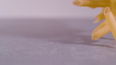 Süper Yavaş Hareketler, Yaklaş, Sonda lensleri: Gri arka planda yayılmış makarna pennette rigate. Makarnanın sağ tarafı ağır çekimde dönüyor. Uçan İtalyan makarnasının detaylı görüntüsü.