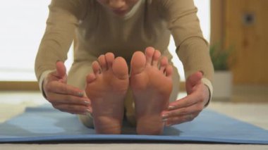 Asyalı kadının öne doğru yoga pozisyonu alıştırması yaparken ön görüntüsü. Mavi yoga minderinde vücut esneme hareketleri yapan genç bir kadın. Canlılık ve esneklik için sağlıklı kapalı aktivite