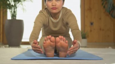PORTRAIT Güzel genç Asyalı kadın kameraya gülümsüyor. Filipinli genç bir kadın mindere oturmuş yoga pozu veriyor. Esneklik ve rahatlama için ev sporu egzersizi