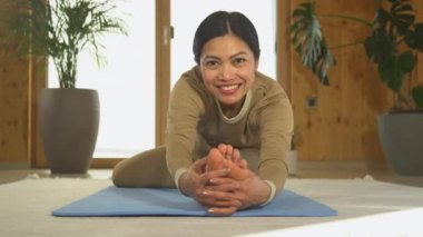 Kameraya bakarken dizlerinin üstüne çöküp yoga pozu veren mutlu, genç Asyalı kadın. Genç bir kadın vücut esneme hareketleri yapıyor. Rahatlama ve esneklik için sağlıklı aktivite.