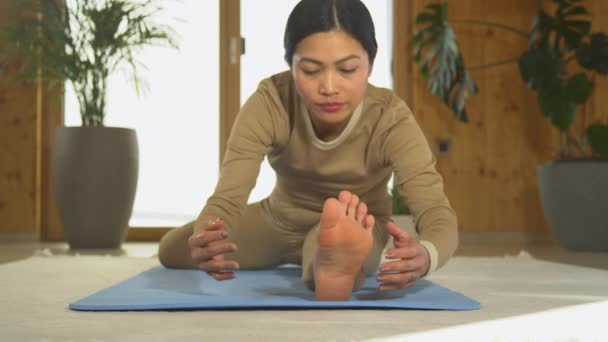 亚洲女子练习坐姿与膝瑜伽的前景 年轻女性在蓝色瑜伽垫上做身体伸展运动 促进放松和灵活性的健康室内活动 — 图库视频影像