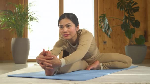 静坐射击 亚洲女人坐在蓝色垫子上叠起瑜伽姿势 沉思冥想 年轻的菲律宾人做着从头到脚的瑜伽姿势 促进放松和灵活性的健康室内活动 — 图库视频影像
