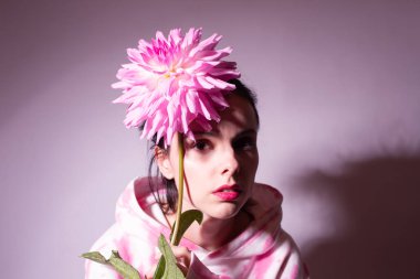 Pembe kapüşonlu kadın elinde pembe bir çiçek tutuyor.