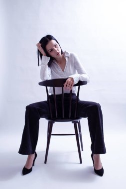 Beyaz gömlekli ve siyah pantolonlu bir kadın sandalyede oturuyor.