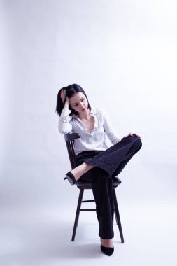 Beyaz gömlekli ve siyah pantolonlu bir kadın sandalyede oturuyor.