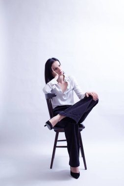 Beyaz gömlekli ve siyah pantolonlu bir kadın sandalyede oturuyor.