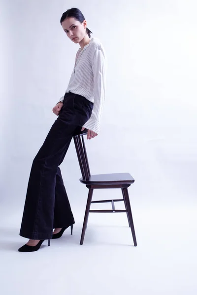 woman in white shirt and black trousers sits on a chair