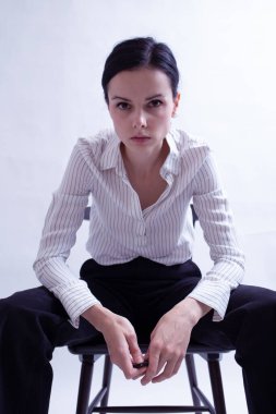 Beyaz gömlekli ve siyah pantolonlu bir kadın sandalyede oturuyor.