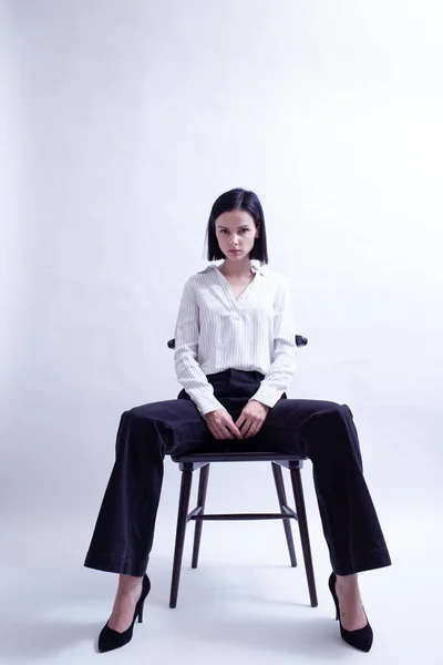 woman in white shirt and black trousers sits on a chair