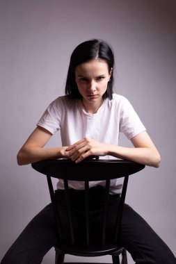 Beyaz tişörtlü kız stüdyoda bir sandalyede oturuyor.