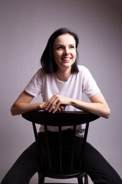 Beyaz tişörtlü kız stüdyoda bir sandalyede oturuyor.