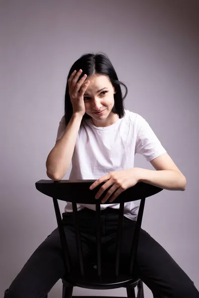 girl in a white t-shirt sits on a chair in the studio