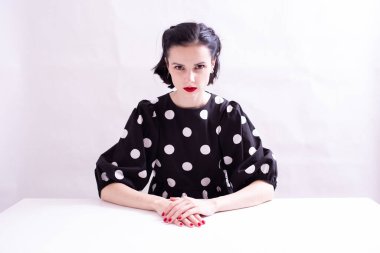 Kırmızı dudaklı puantiyeli güzel bir kadın beyaz bir masada beyaz arka planda oturuyor.