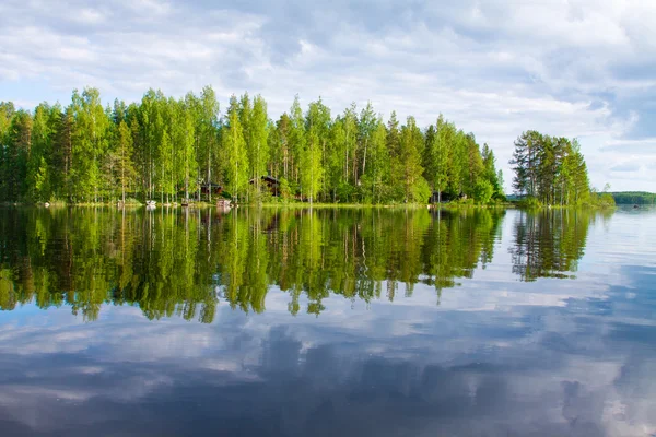 Bos met rode huis aan de oever van het meer, hemel met wolken weerspiegelen — Stockfoto