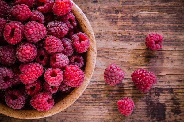 organic raspberries in a bowl on wooden background