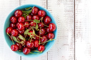 Beyaz ahşap zemin üzerinde mavi bir kase kiraz