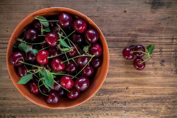 Ripe cherries with leaves in bowl on old wooden rustic backgroun — Stock Photo, Image