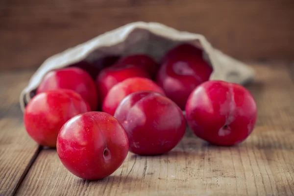Red plums in a bag on an old rustic wooden background — Stock Photo, Image